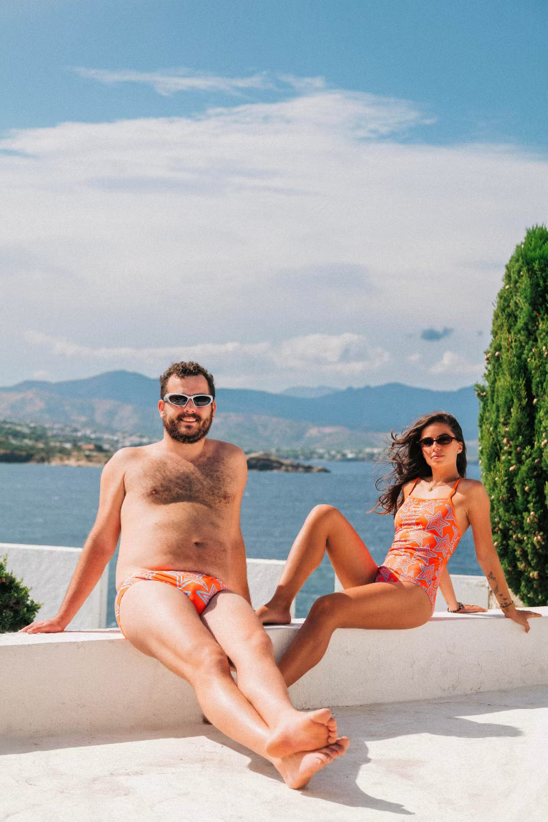 Man and women wearing orange star swimwear by the water 