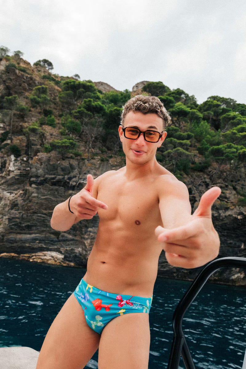 Man wearing blue swimwear briefs with dogs on them by the water 