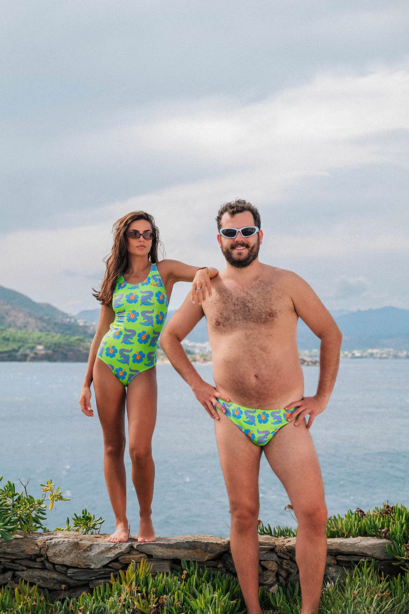 Man and women wearing green swimwear with a crocodile floral print by the water 