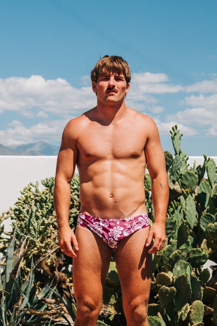 Man wearing a pink swimsuit with cacti and blue sky in the background
